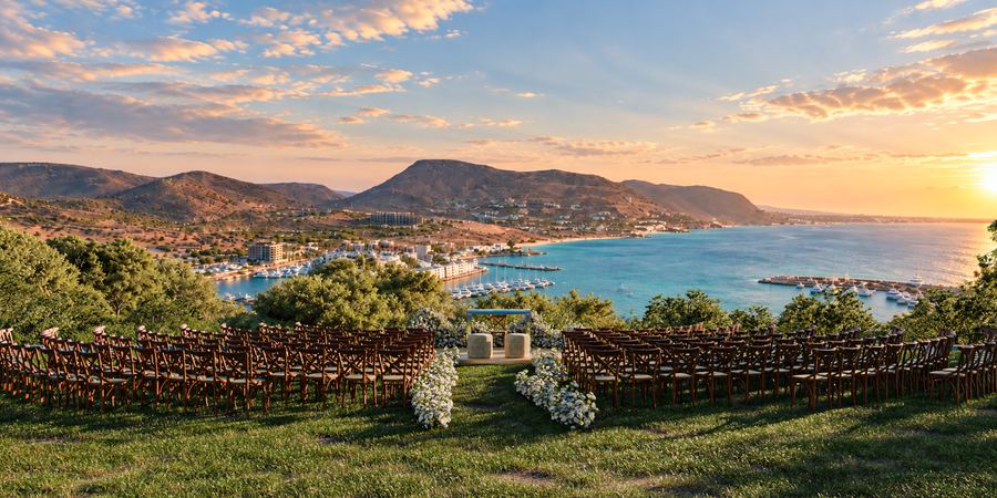 Ceremonia frente al mar al atardecer con sillas de madera y flores blancas